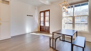 A spacious room with wooden floors, a large window with a view, and a modern table. - Fire Pit + Mountain Views! Waynesville Escape (Clyde)