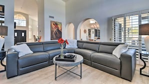 Un salon moderne doté d’un grand canapé d’angle, d’une table basse ronde et d’une grande fenêtre offrant une vue sur la ville.