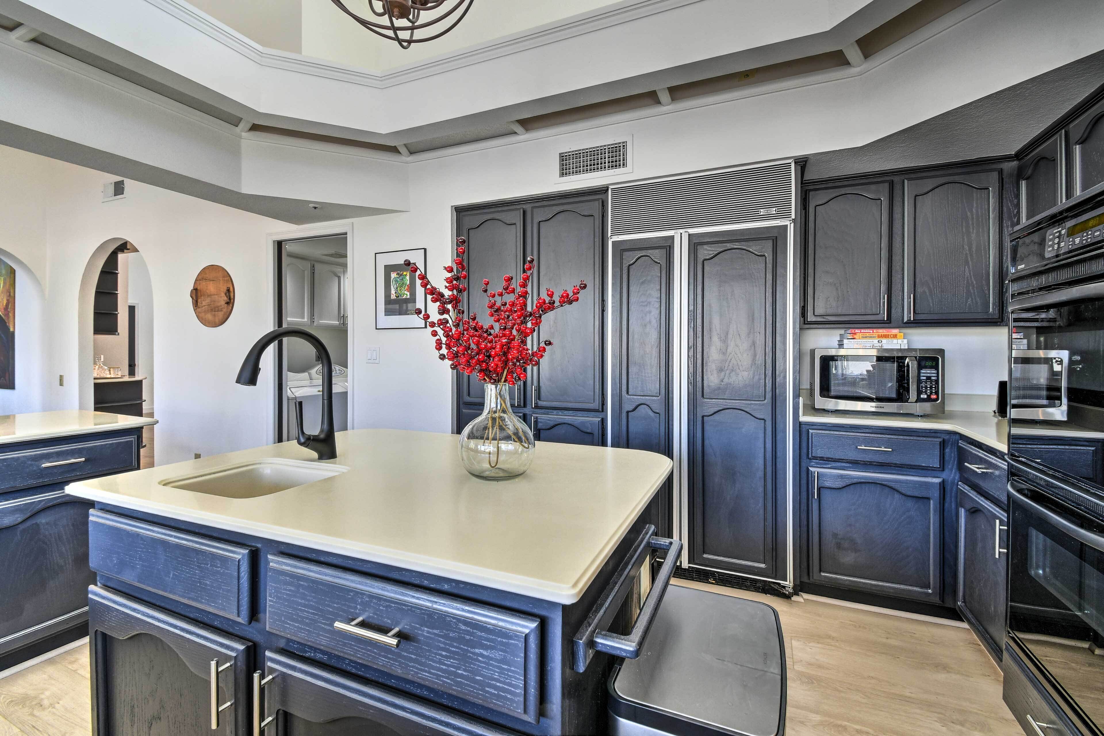 A modern kitchen with dark cabinetry, a central island with a sink, and built-in appliances including a microwave and oven.