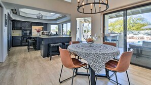 Une cuisine moderne avec des meubles de couleur sombre, un îlot central et un coin repas comprenant une table ronde et des chaises.