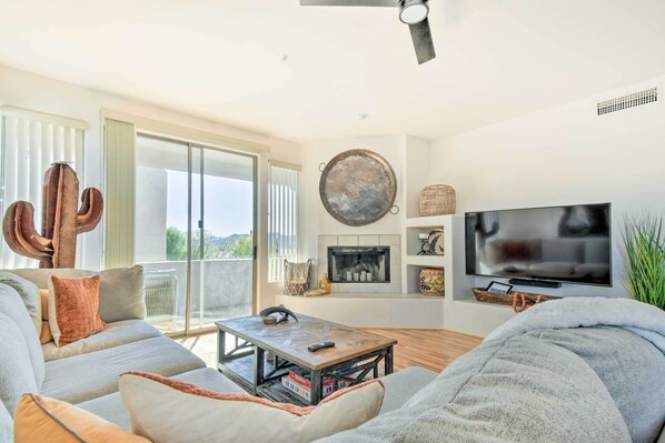 A spacious living room with a large flat-screen TV, a fireplace, and a cactus sculpture. - Pool Access: Mountain-view Condo in Fountain Hills (Fountain Hills)