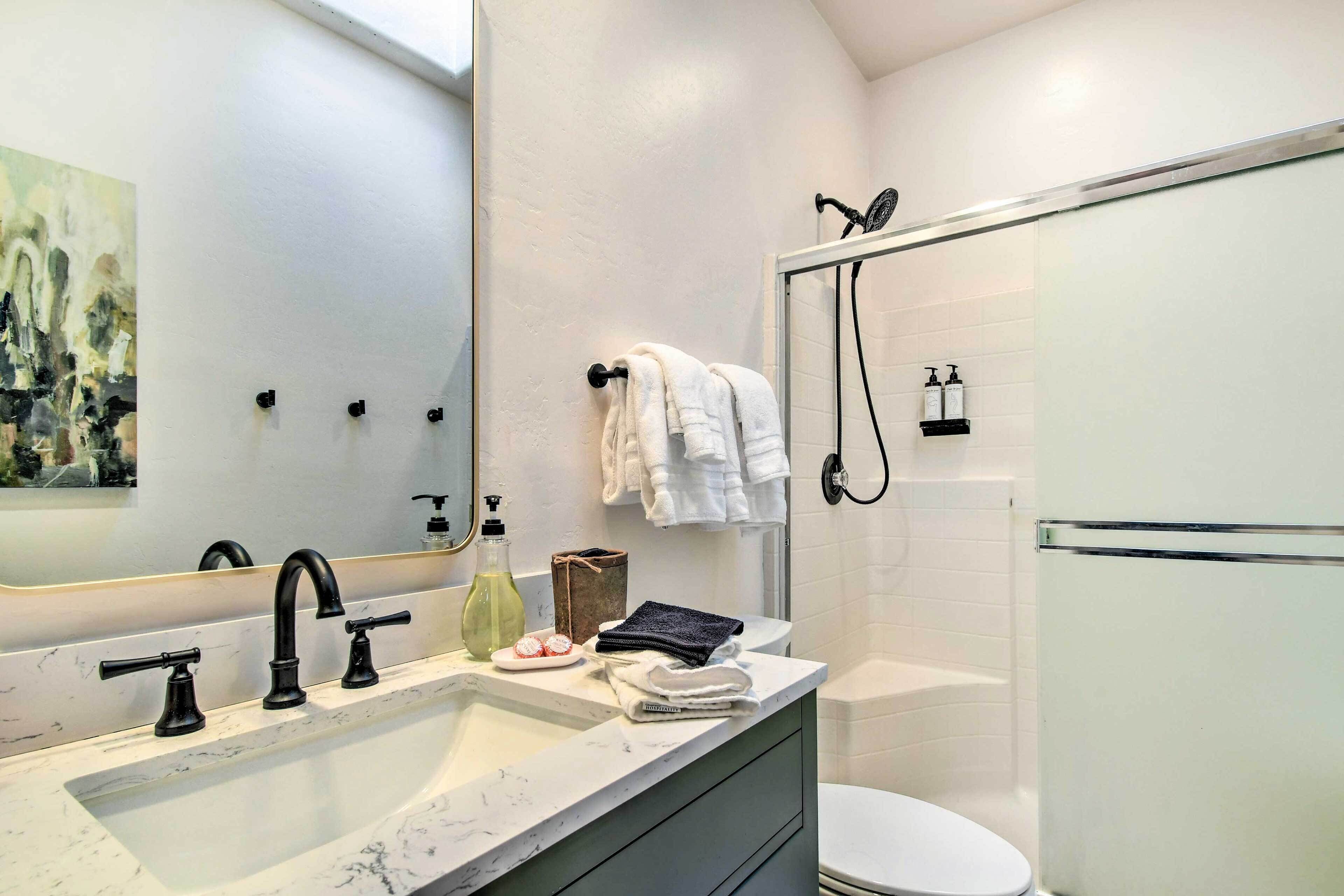 A modern bathroom with a white sink, black faucets, a large mirror, and a glass shower enclosure.