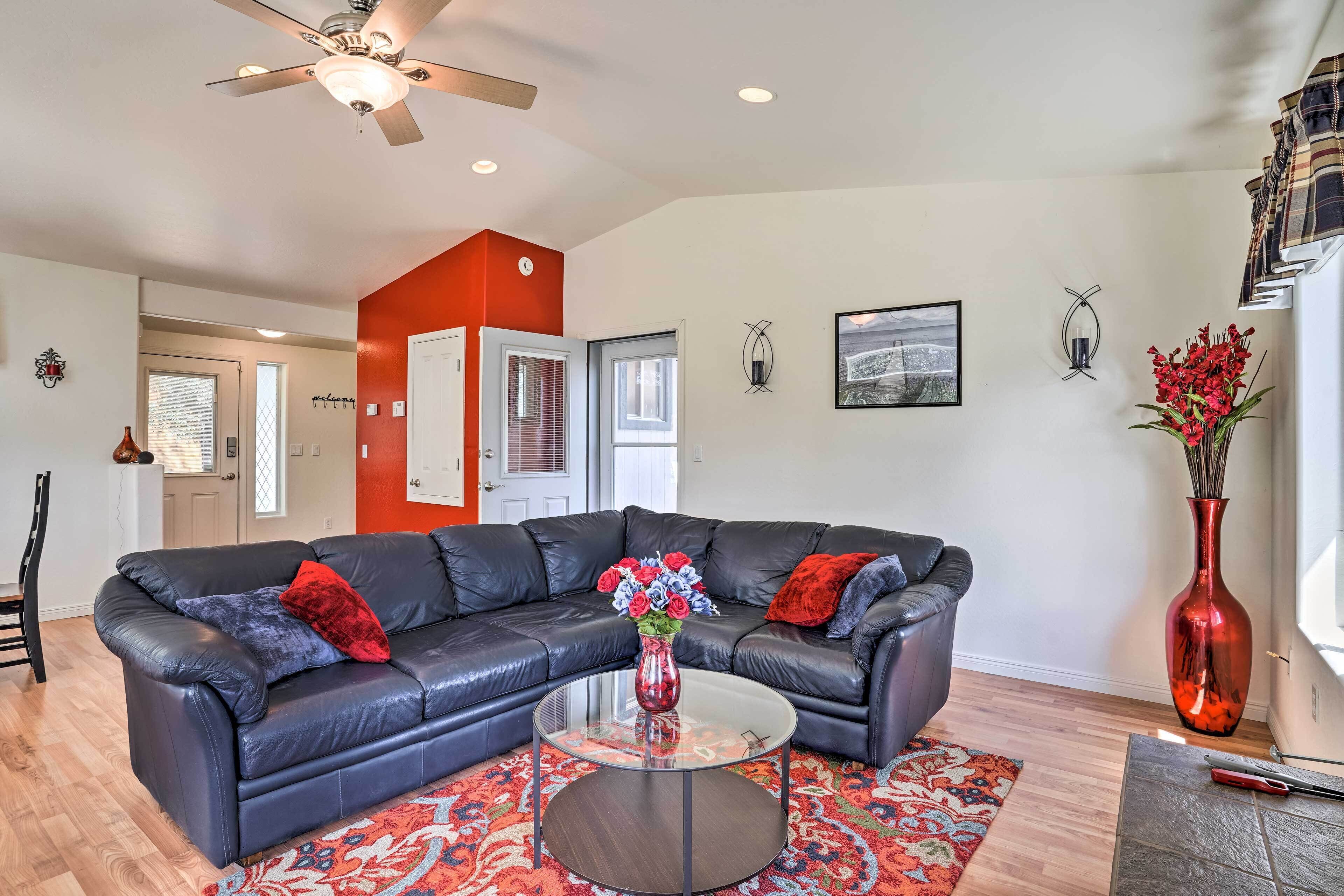 A living room with a black leather sofa, a glass coffee table, and a red vase with flowers.