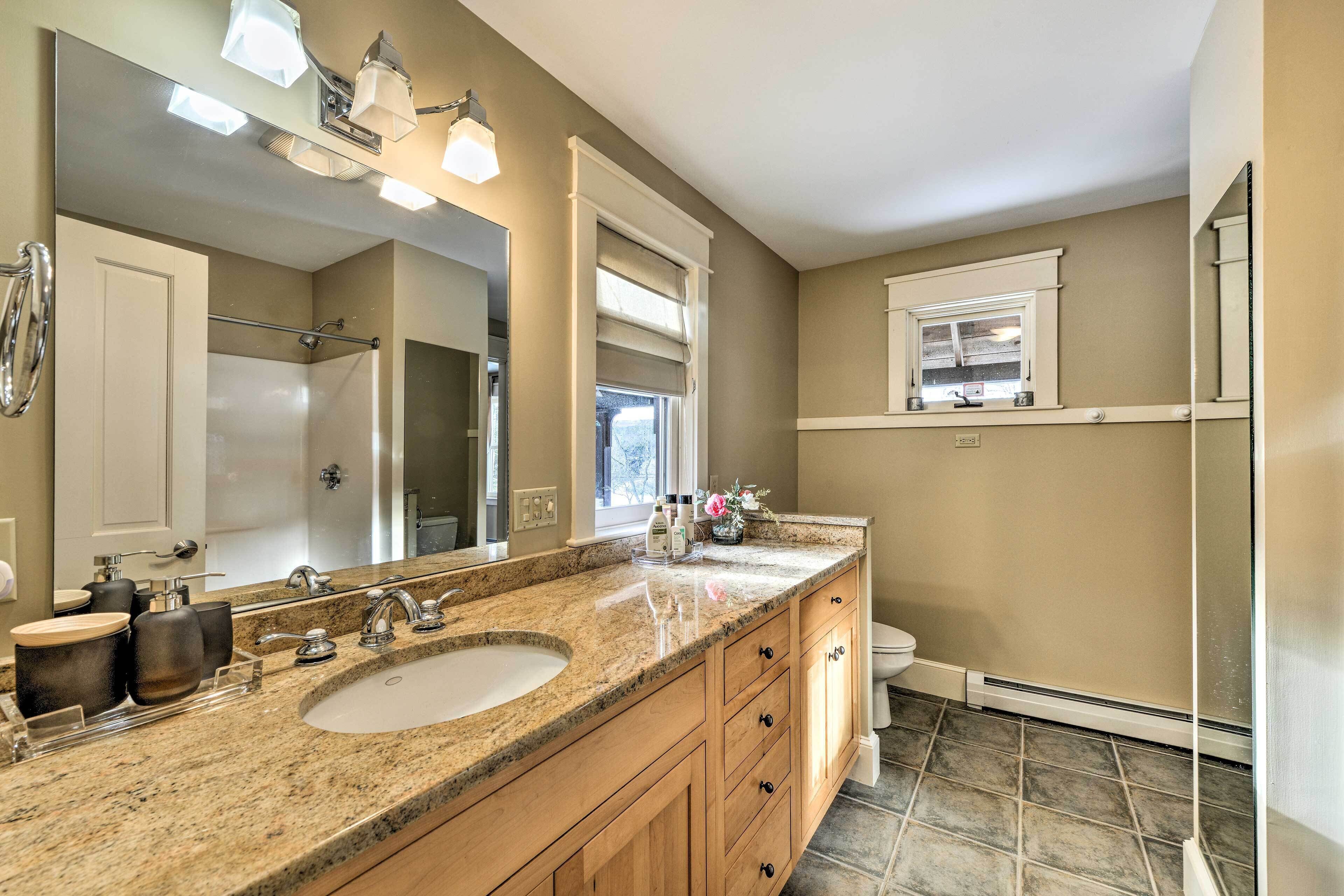 A bathroom with a large mirror, two sinks, wooden cabinets, and a window.