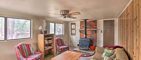 Un salon chaleureux avec une cheminée, des fauteuils à carreaux, une table basse en bois et un ventilateur de plafond.