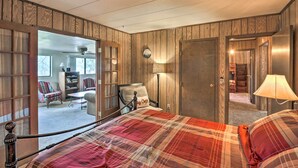 Un dormitorio con colcha a cuadros, paredes de madera y vistas a una sala de estar con sofá y sillones.