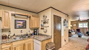 Una cocina con gabinetes de madera, lavavajillas, fregadero y cafetera. Hay una puerta con perchero y un marco de fotos en la pared.