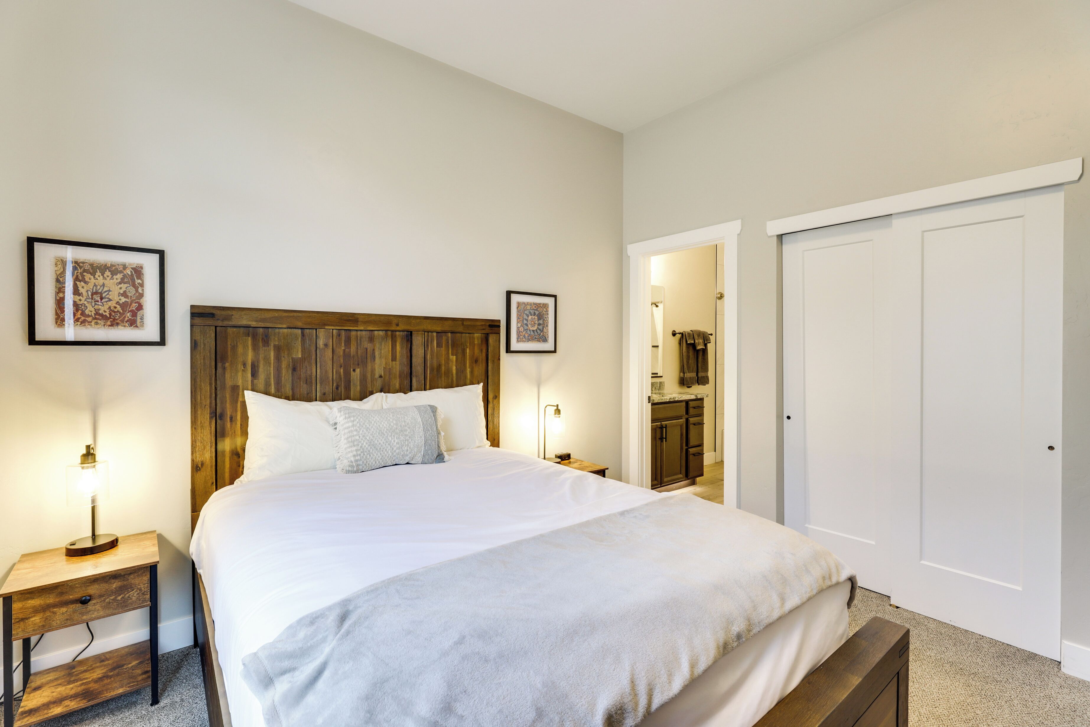 A neatly made bed with a wooden headboard, two bedside tables with lamps, and framed pictures on the wall.