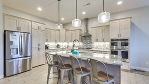 A modern kitchen with stainless steel appliances, a large island with bar stools, and pendant lighting. - Stunning Grand Junction Home Near Downtown! (Grand Junction)