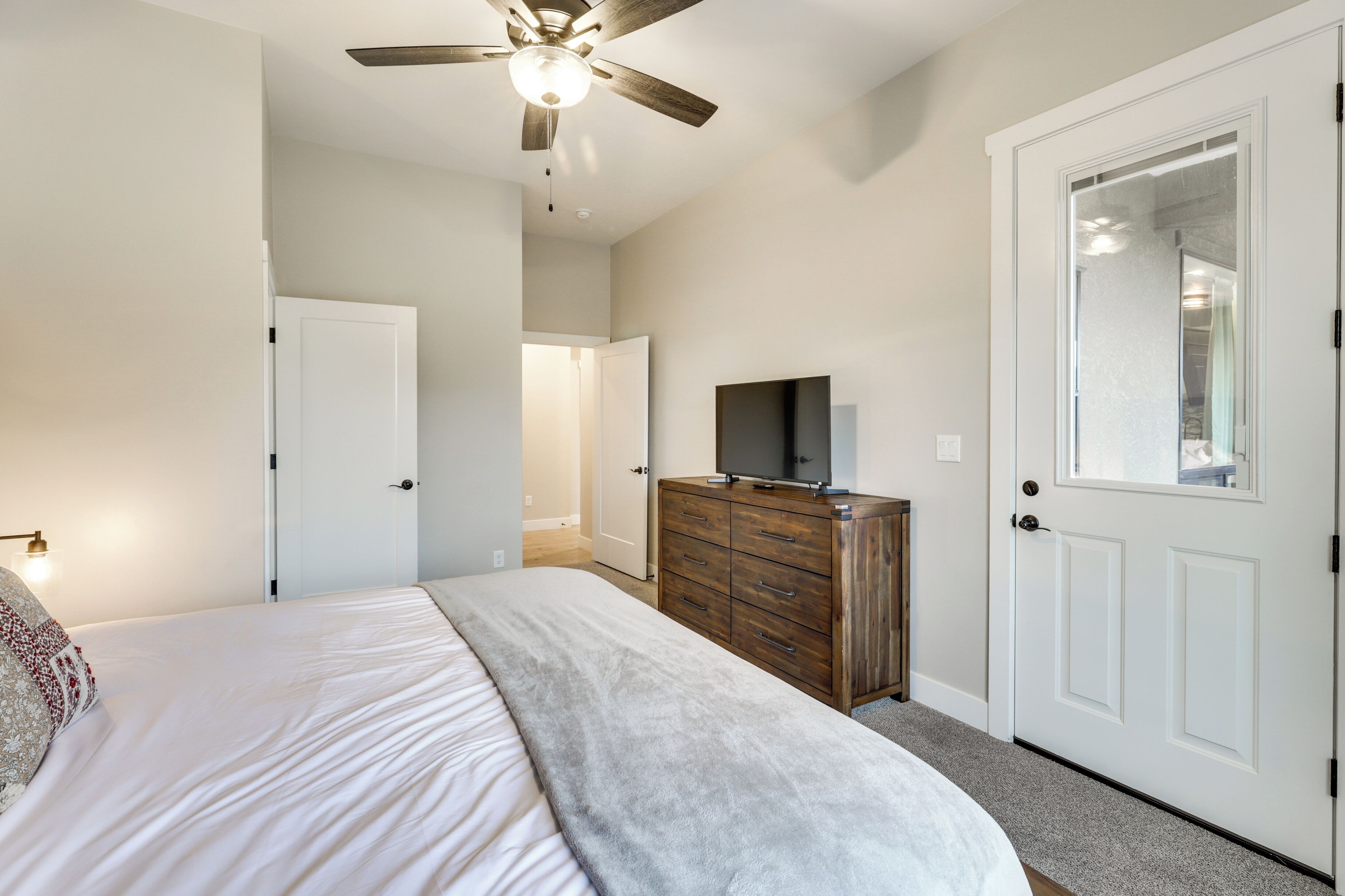 Un dormitorio con cama, cómoda, televisor, ventilador de techo y puerta.