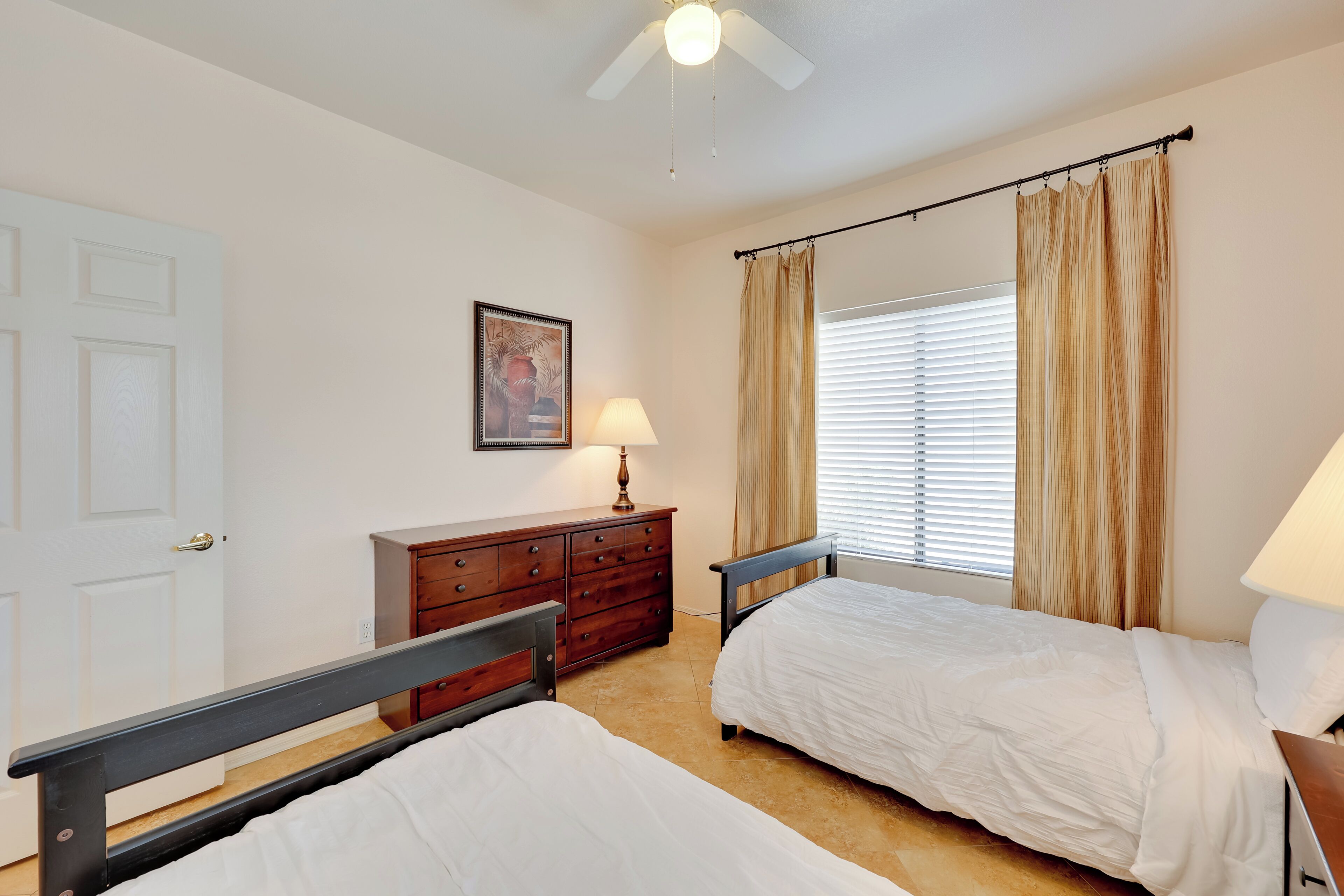 A bedroom with two beds, a dresser, a ceiling fan, and a window with curtains.