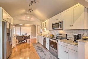 A modern kitchen with white cabinets, a stainless steel refrigerator, a microwave, and a stove. There is a dining area with a table and chairs. - Luxe Lyndon Home < 11 Mi to Dtwn Louisville! (Louisville)