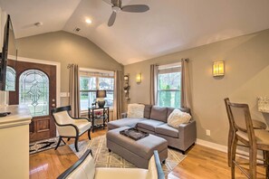 A spacious living room with a grey sectional sofa, a white armchair, and a wooden dining table.