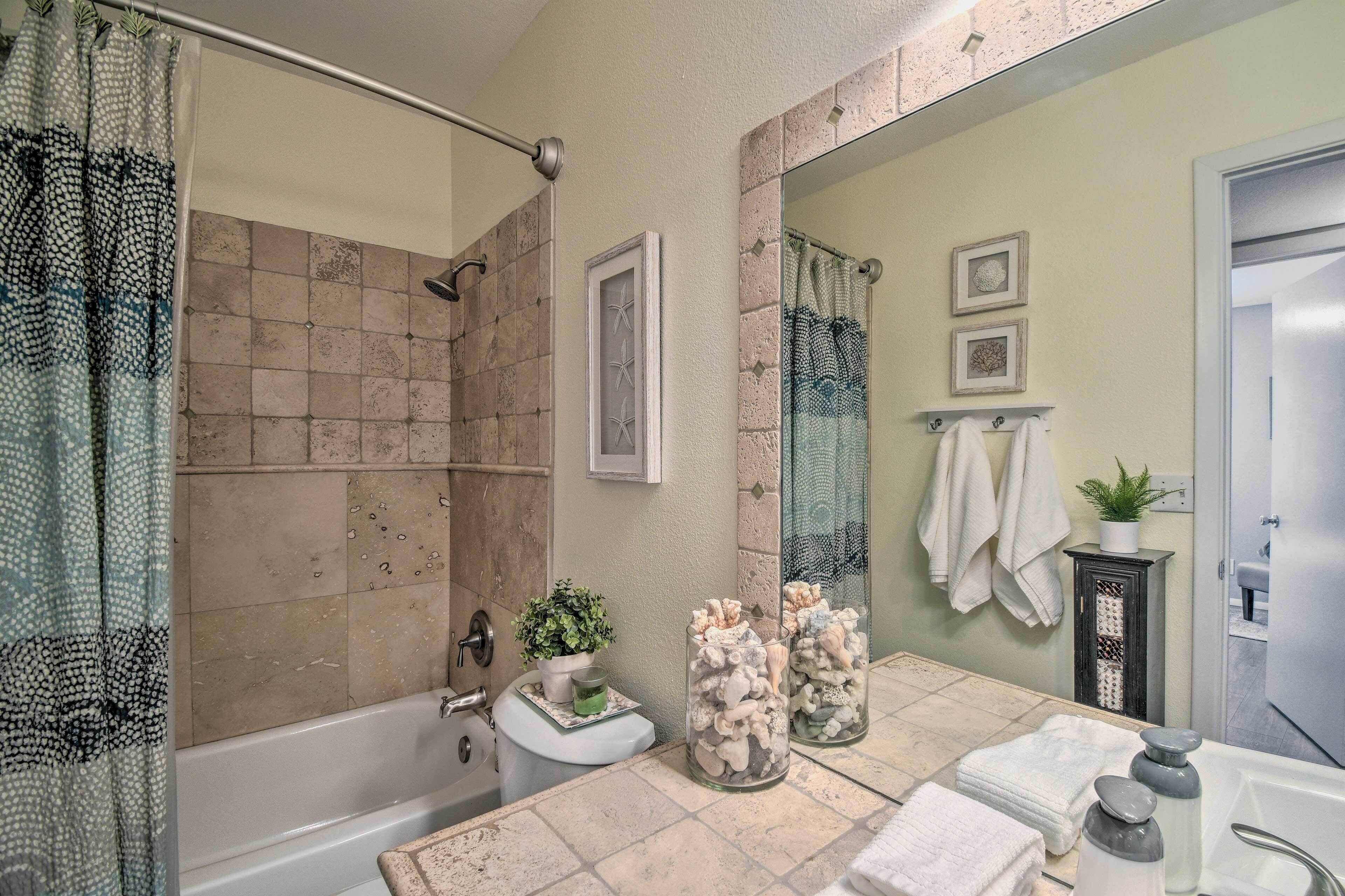 A bathroom with a bathtub, a shower area, a sink with a mirror, and a toilet. There are decorative jars with shells and a small plant on the sink.