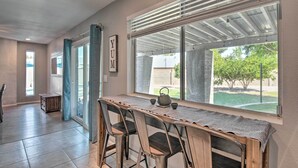 A dining area with a long table, chairs, and a view through large windows. - Near Golfing: Mesa Escape w/ Pool & Yard (Mesa)