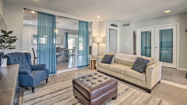 A modern living room with a sofa, ottoman, and armchair, a dining area in the background, and a sliding glass door leading to a balcony. - Near Golfing: Mesa Escape w/ Pool & Yard (Mesa)