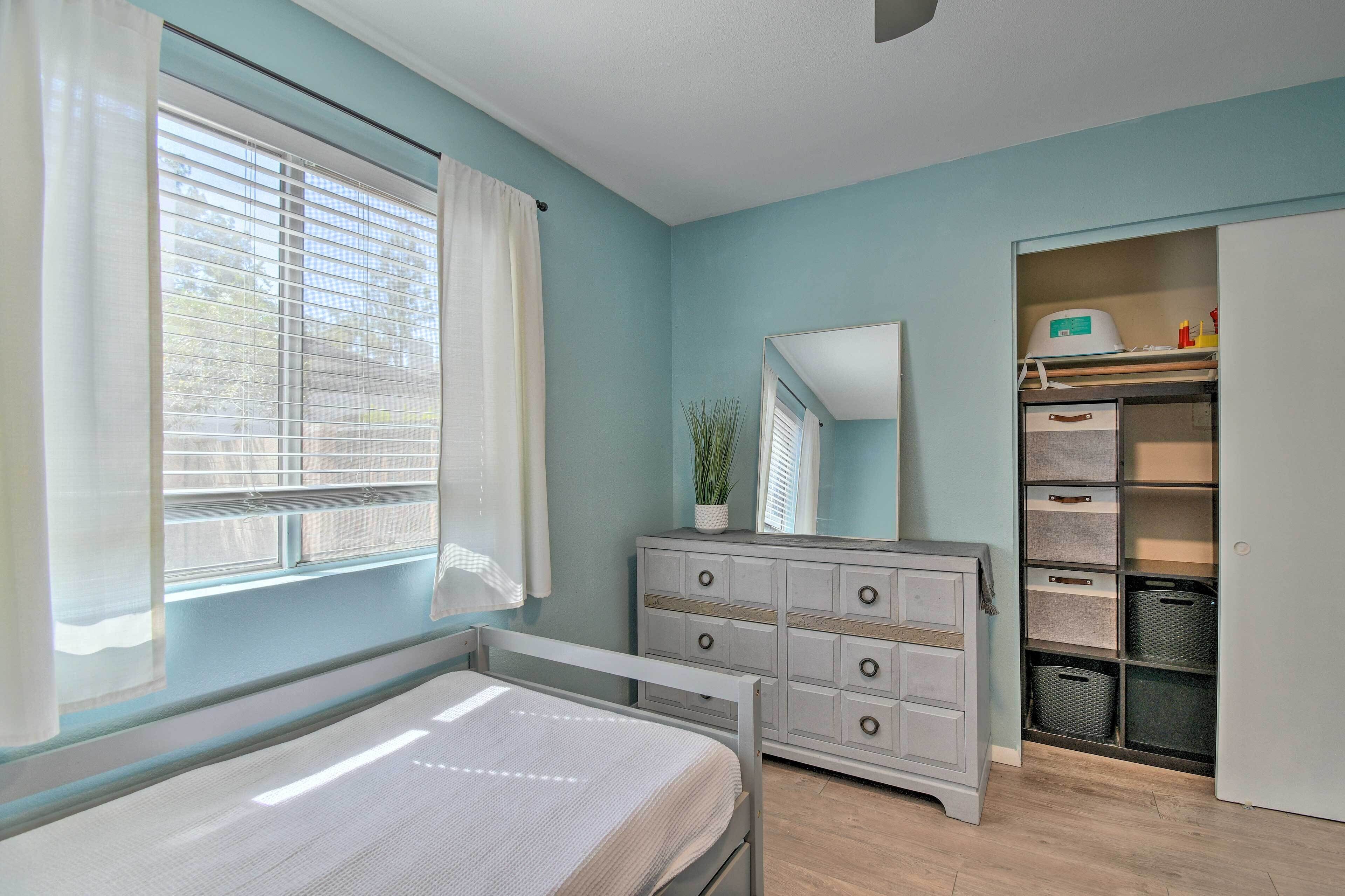 A bedroom with a bed, a dresser, a mirror, and a closet with storage bins.