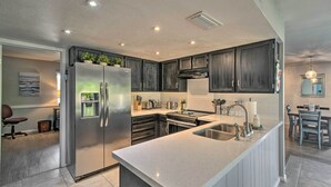 A modern kitchen with dark cabinets, a stainless steel refrigerator, and a large island with a sink. - Near Golfing: Mesa Escape w/ Pool & Yard (Mesa)