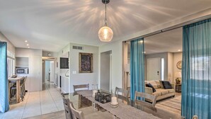 A modern dining area with a glass table, wooden chairs, and a hanging light fixture. - Near Golfing: Mesa Escape w/ Pool & Yard (Mesa)
