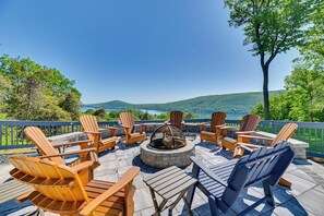 An outdoor deck with Adirondack chairs, a fire pit, and a scenic view of a lake and hills. - Finger Lakes Vacation Rental w/ Hot Tub & Pool (Naples)