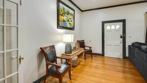 Quarto com piso de madeira, porta branca, quadro emoldurado e duas cadeiras de madeira.
