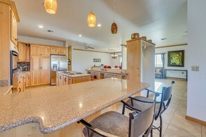 A spacious kitchen with granite countertops, wooden cabinets, and a central island with bar stools. - Private Hot Tub & Epic Views in Superstition Mtns! (Apache Junction)