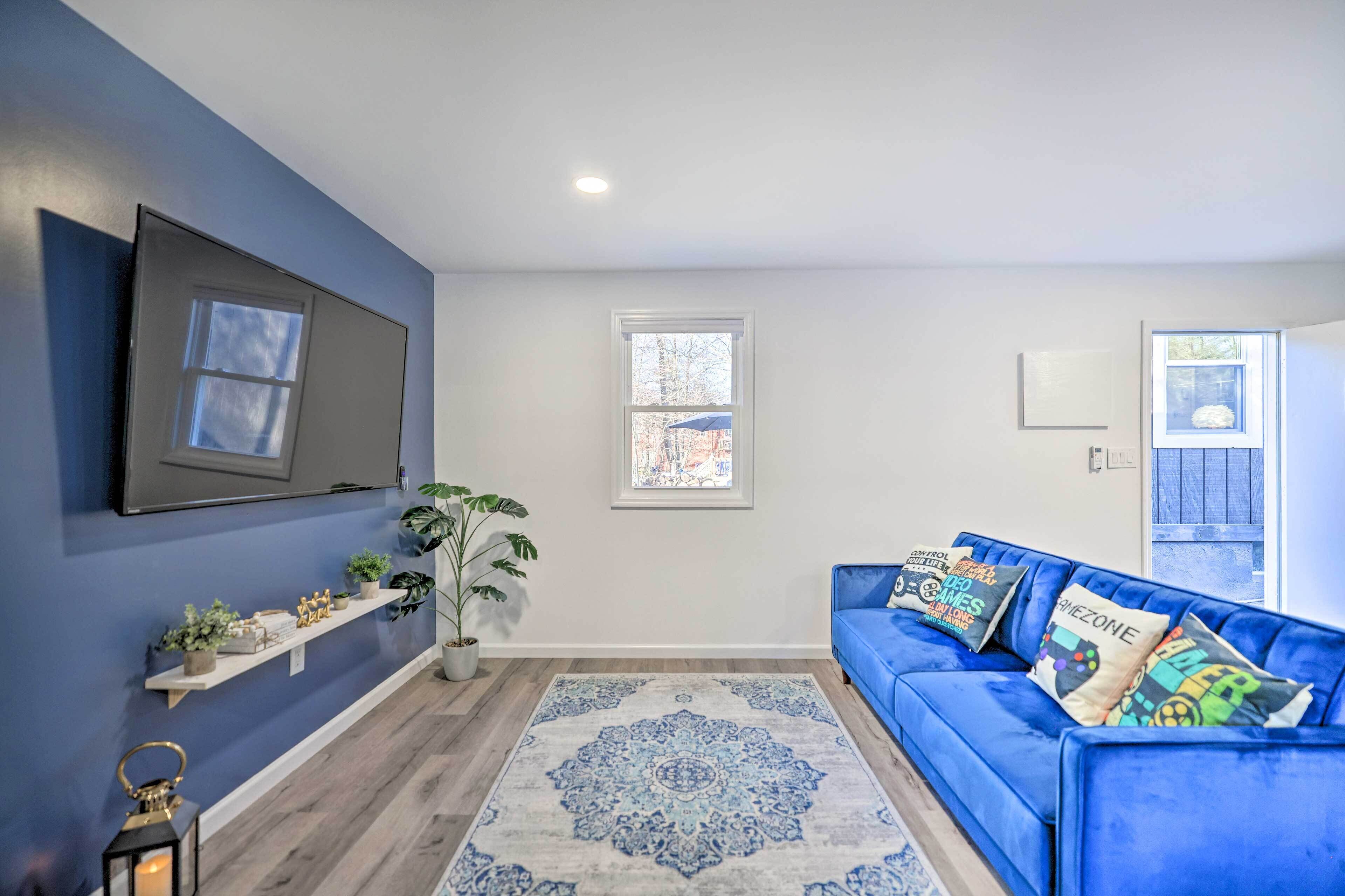 Un salon avec un canapé bleu, un téléviseur à écran plat, un tapis à motifs et une plante en pot.