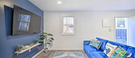Un salon avec un canapé bleu, un téléviseur à écran plat, un tapis à motifs et une plante en pot.