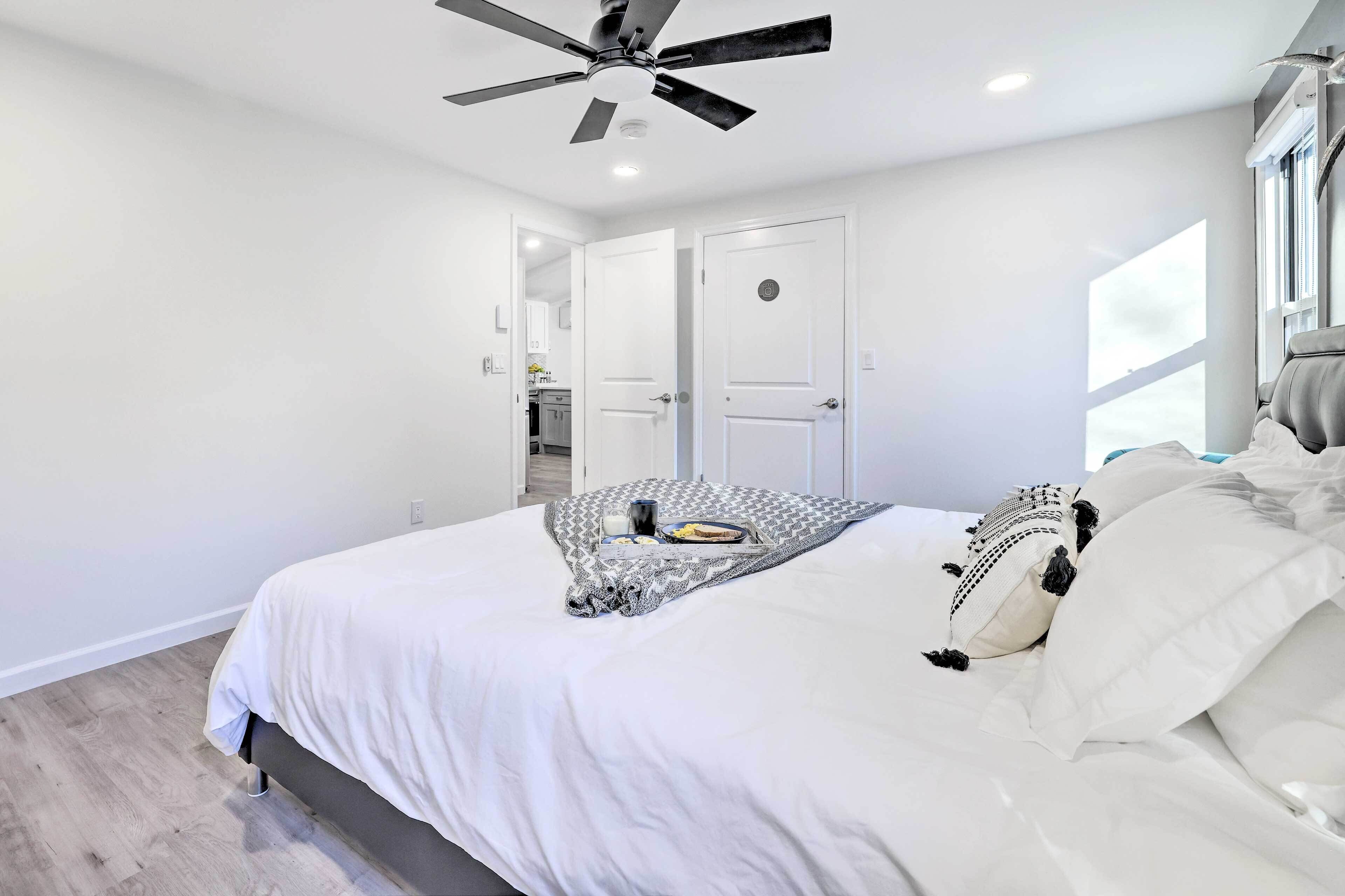 A bedroom with a bed, white walls, a ceiling fan, and a window.