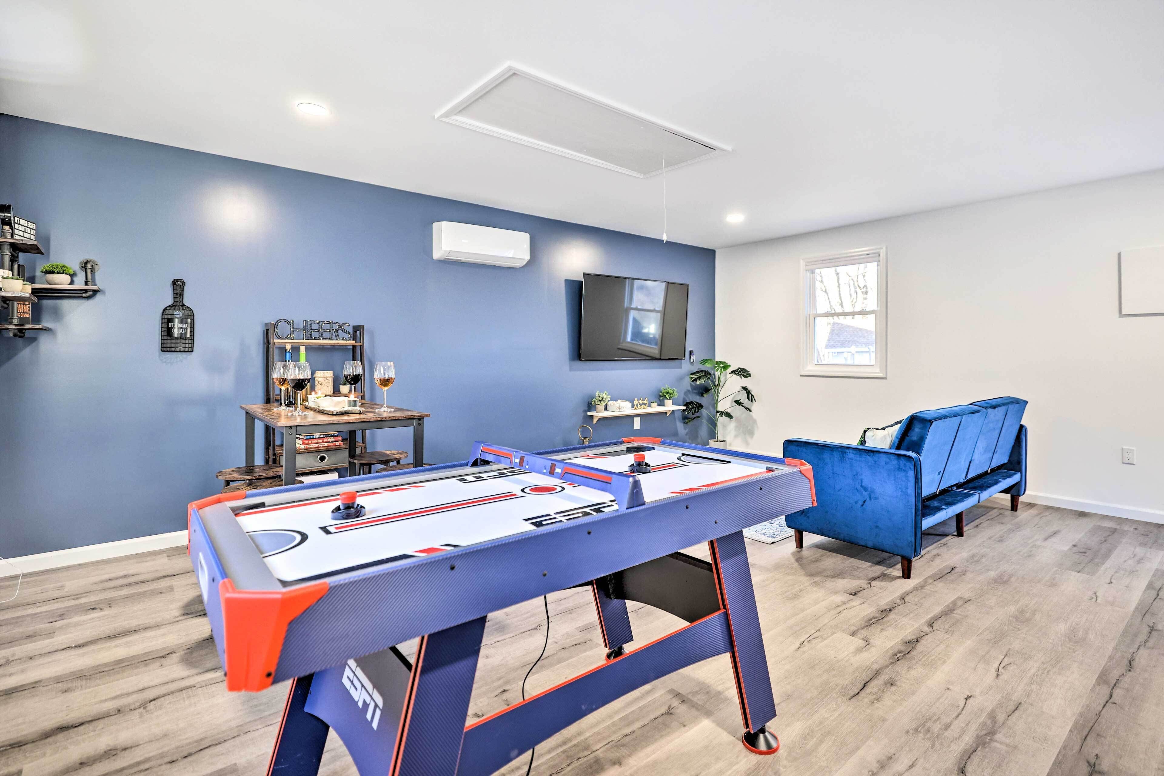 Une pièce avec une table de baby-foot, un canapé bleu, un téléviseur fixé au mur et une fenêtre.