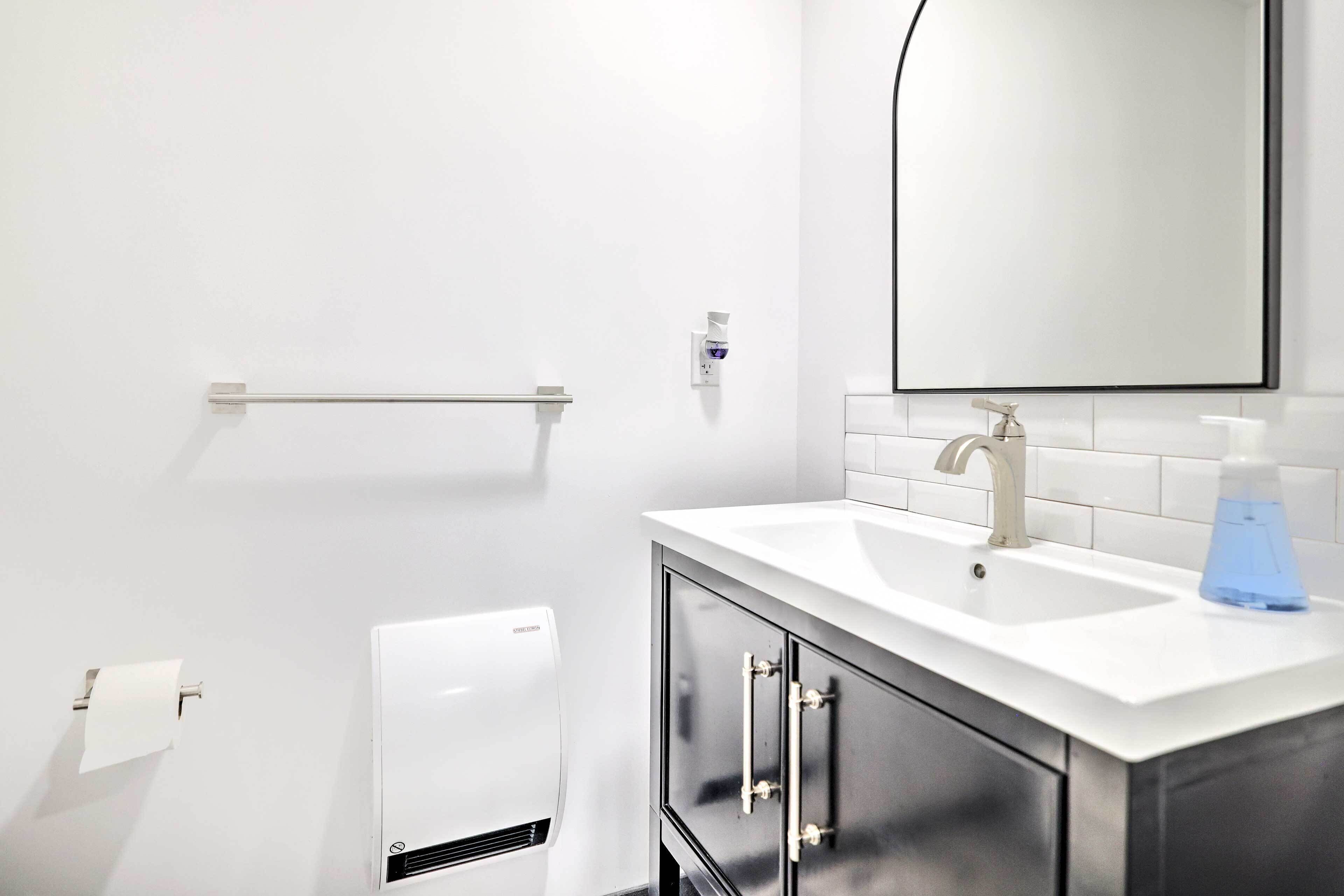 A modern bathroom with a white sink, a mirror, and a hand dryer.
