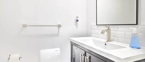 A modern bathroom with a white sink, a mirror, and a hand dryer.