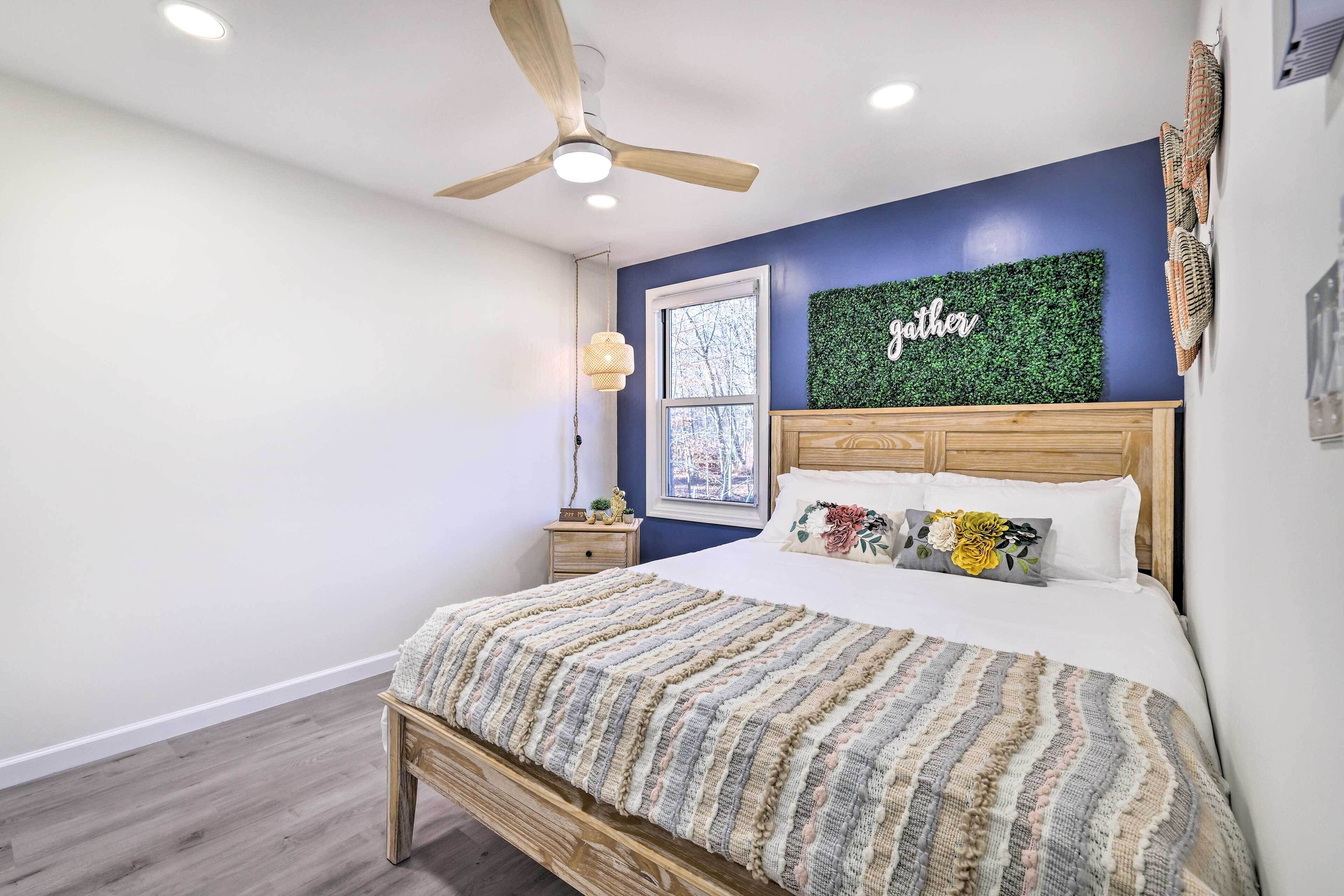A bedroom with a bed, a ceiling fan, a window, and a wall with a green wall hanging.