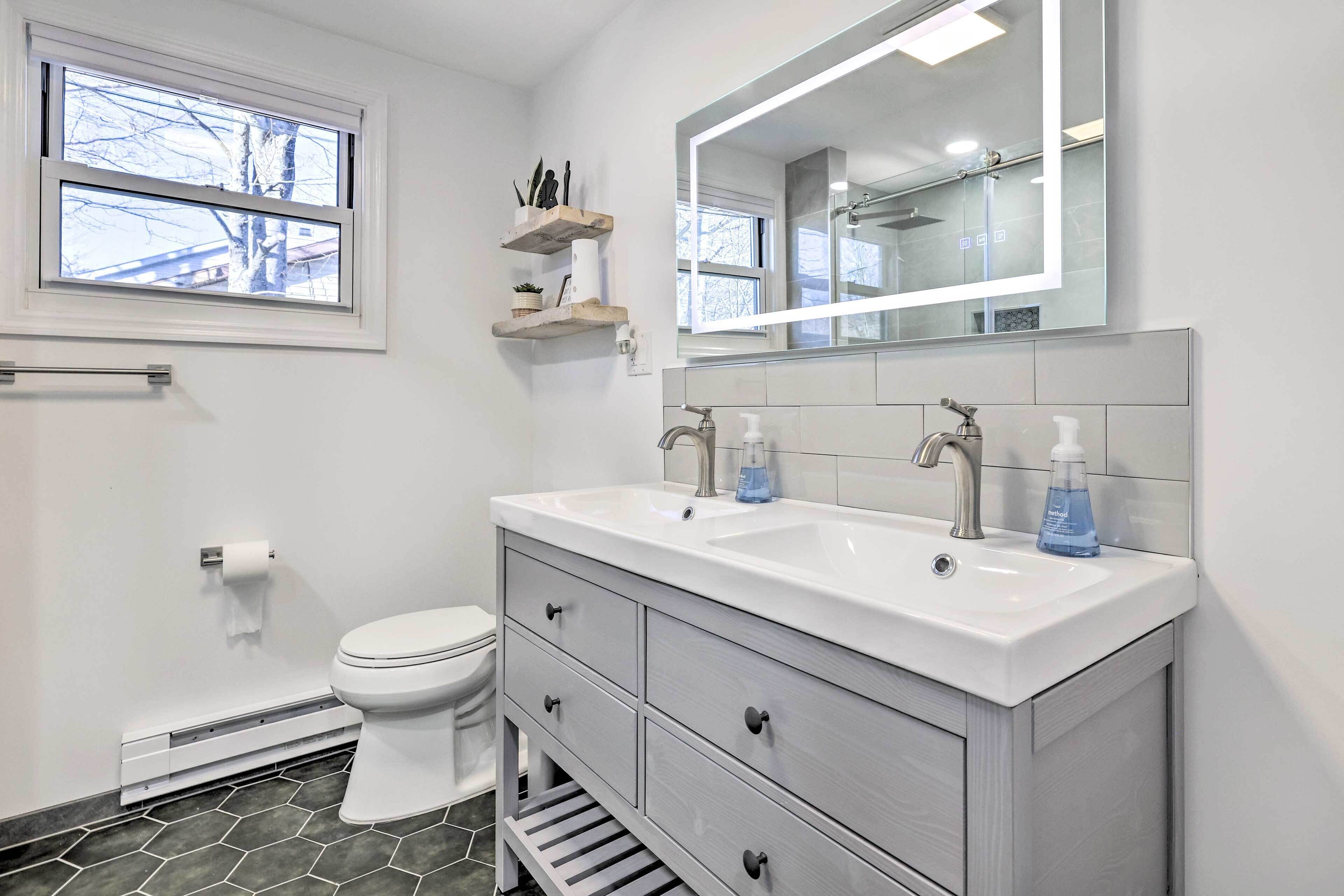 Un baño moderno con tocador blanco, dos lavabos, un espejo grande y un inodoro.