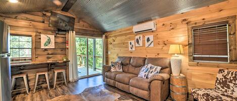 L’intérieur d’un chalet accueillant, avec un plancher en bois, un canapé en cuir, une petite table et un ventilateur de plafond.