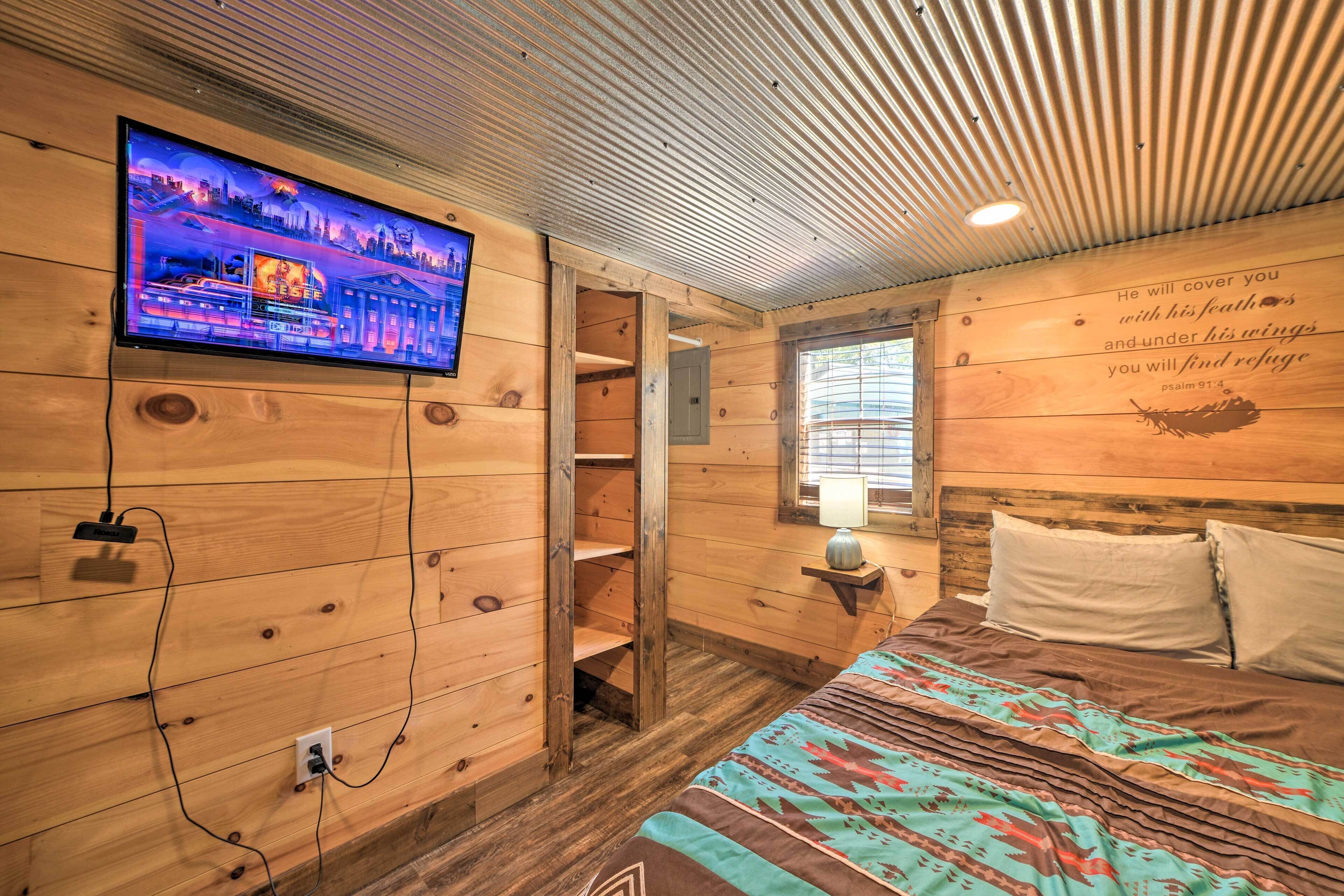 Una habitación de cabaña de madera con una cama, un televisor montado en la pared y un versículo bíblico en la pared.
