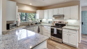 A kitchen with white cabinets, granite countertops, a built-in oven, and a window with a view of trees. - Deck + Game Room: Lakeside 'blue Jay Chalet' Cabin (Lakeside)