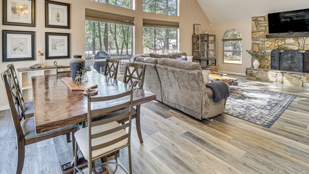 A spacious living room with a large window, a fireplace, and a dining area with a wooden table and chairs. - Deck + Game Room: Lakeside 'blue Jay Chalet' Cabin (Lakeside)
