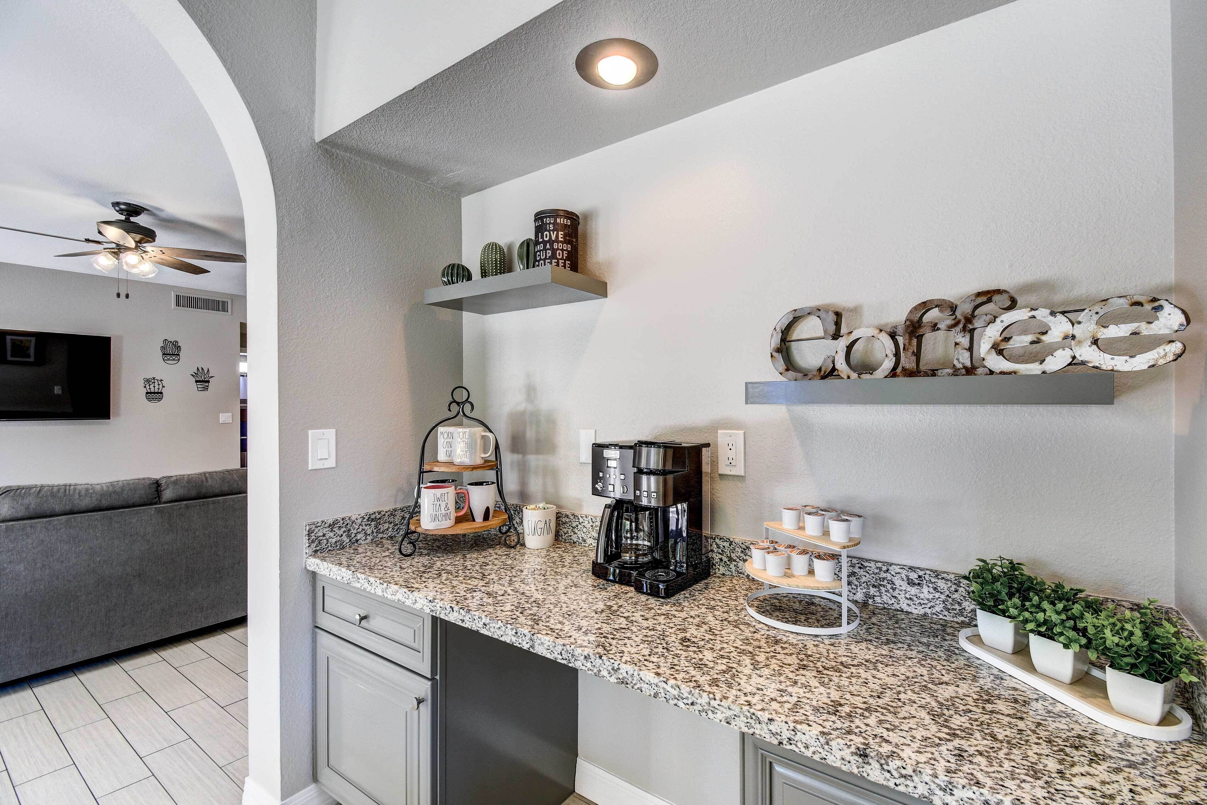 A kitchen with granite countertops, a coffee maker, and decorative items on shelves.