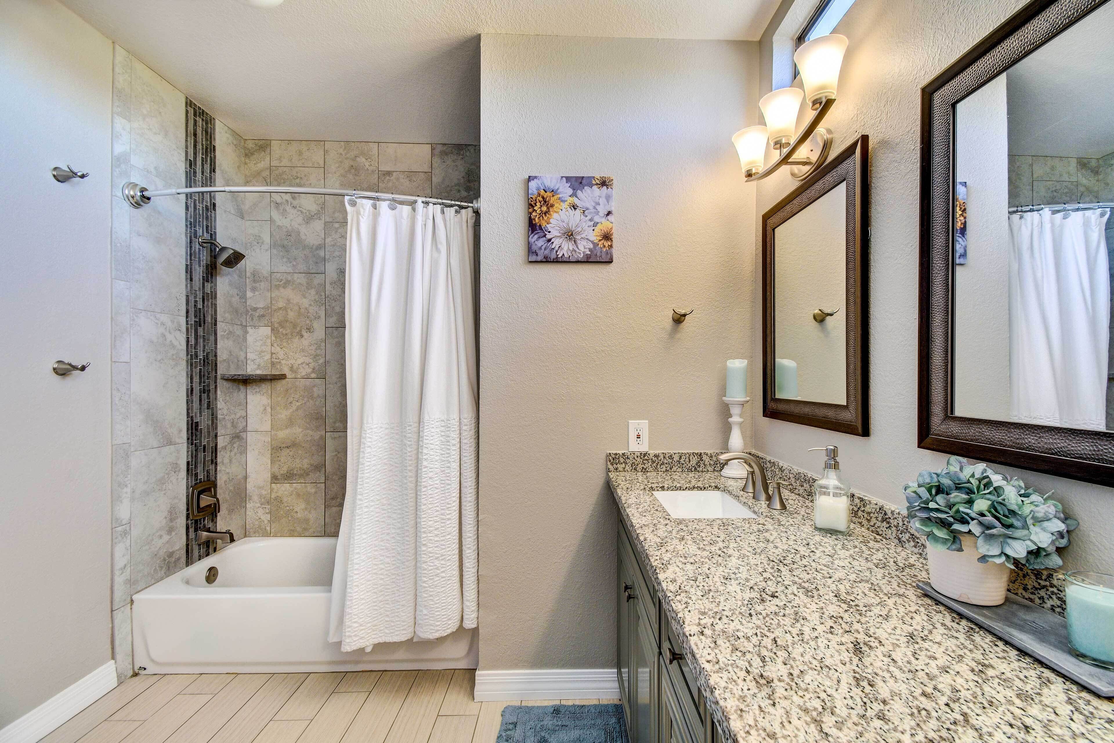 A bathroom with a shower, a sink, a mirror, and a potted plant.