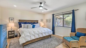 A bedroom with a bed, a chair, a ceiling fan, a window with curtains, and a nightstand with a lamp. - Sunny Phoenix Home w/ Pool + Backyard Oasis! (Phoenix)
