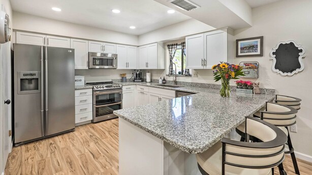 A modern kitchen with white cabinets, stainless steel appliances, a granite countertop, and a bar area with stools. - Sunny Phoenix Home w/ Pool + Backyard Oasis! (Phoenix)