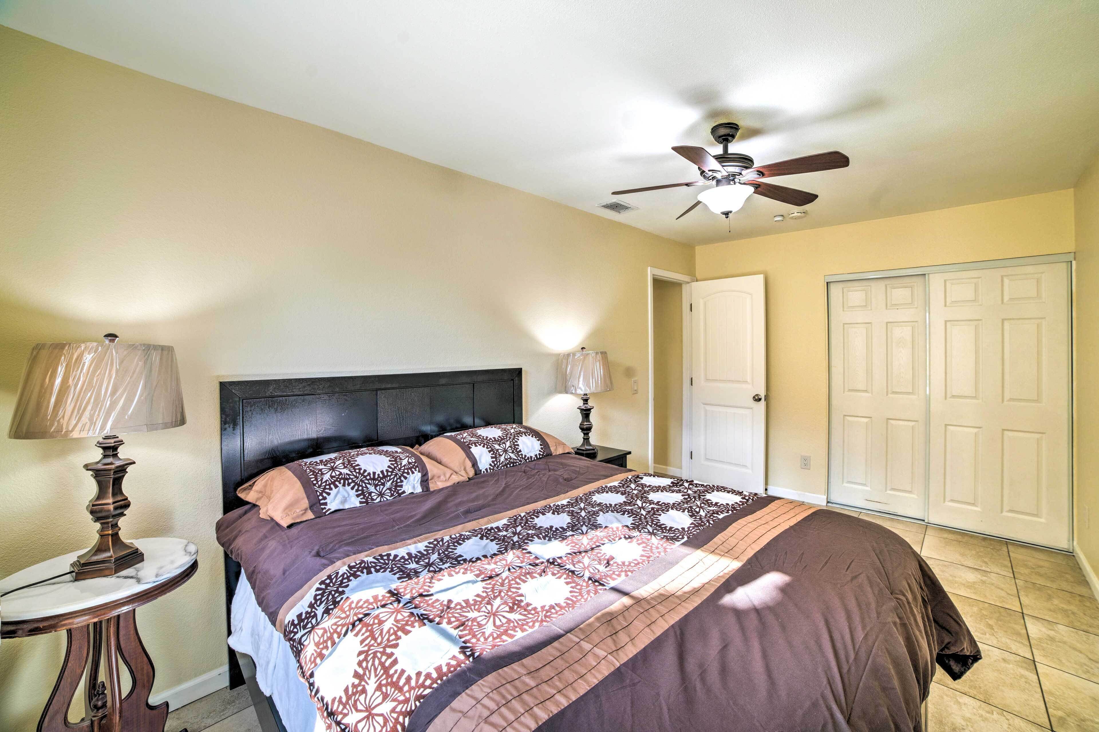 A bedroom with a bed, two bedside lamps, a ceiling fan, and a door.