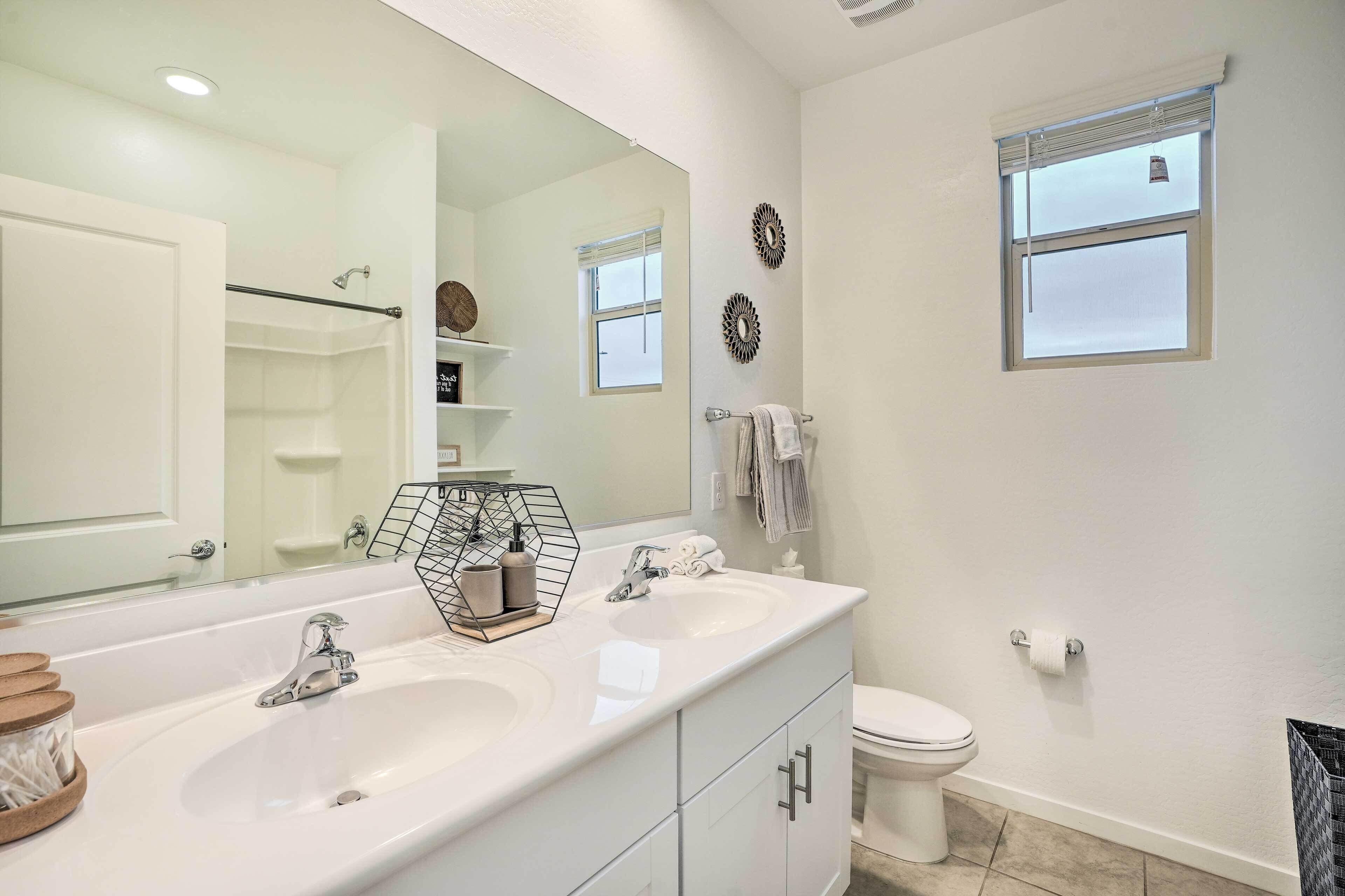 A modern bathroom with a double sink vanity, a large mirror, a toilet, and a window with blinds.