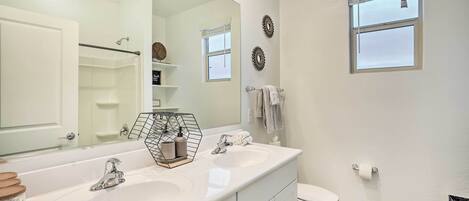 A modern bathroom with a double sink vanity, a large mirror, a toilet, and a window with blinds.