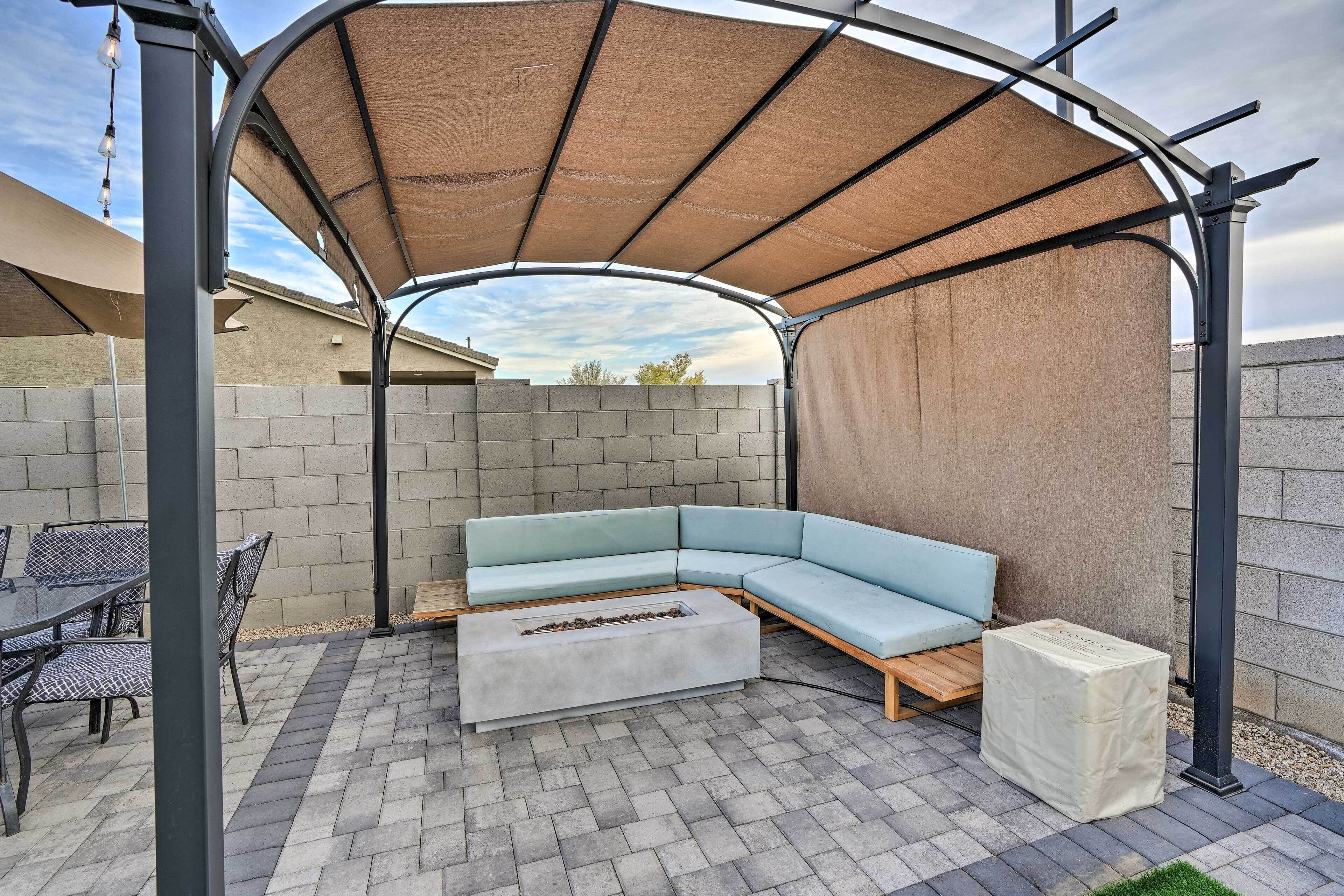 A covered outdoor seating area with a sectional sofa, a fire pit, and a table with chairs.