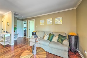 A living room with a sofa, a coffee table, and a tall vase with flowers. There is a door leading to another room, and a small table with a vase and a plant. - Family-friendly Hot Springs Hideaway w/ Yard! (Hot Springs)