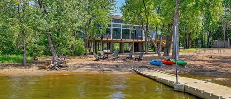 A modern house with a deck extending over a body of water, surrounded by trees.