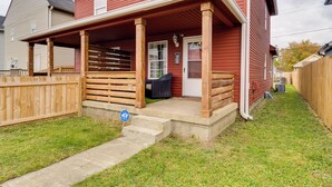 A red house with a porch, a wooden fence, and a grassy yard. - Chic Indianapolis Home w/ Yard Near Downtown! (Indianapolis)