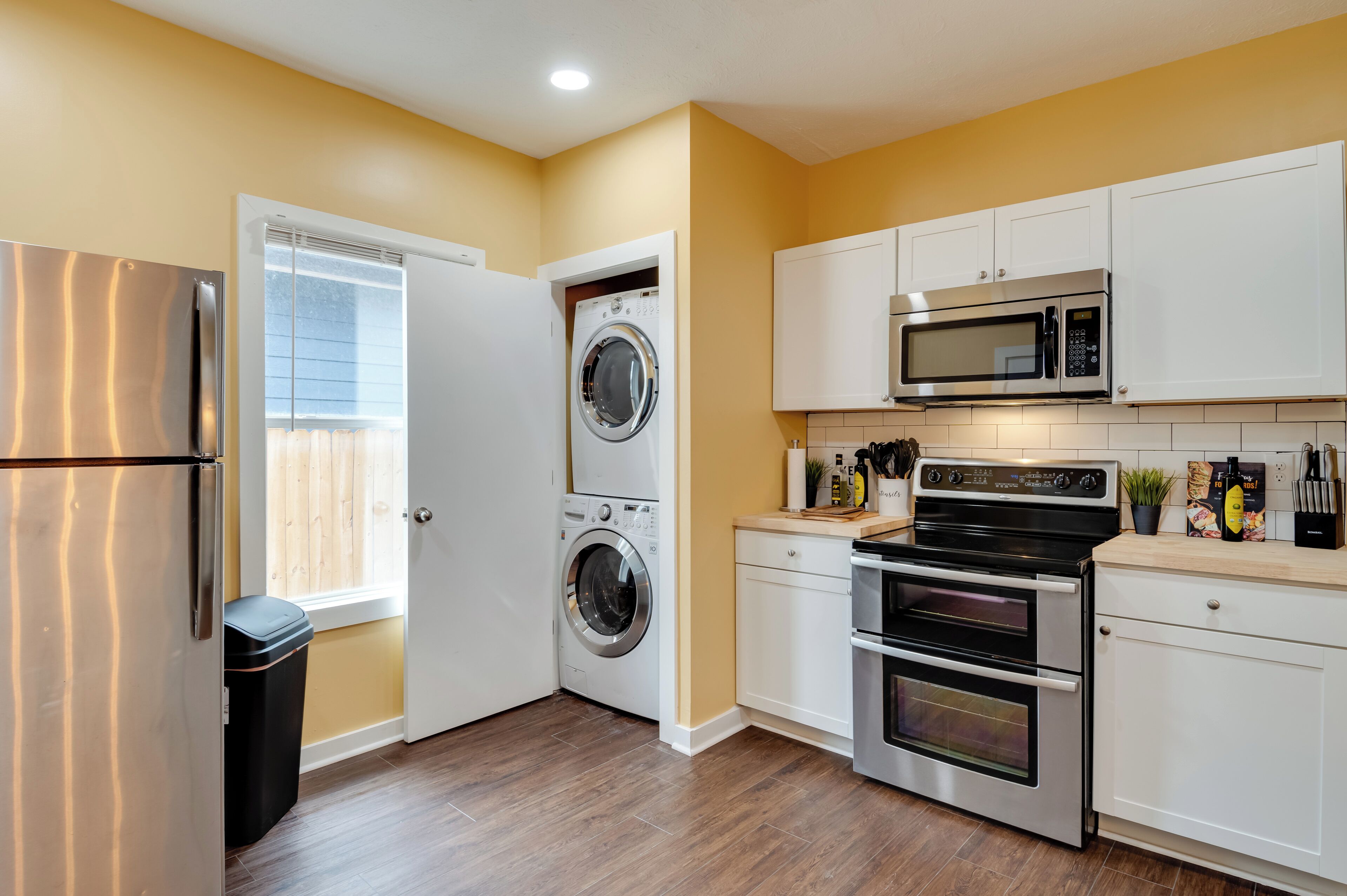 A compact kitchen with a stainless steel refrigerator, a built-in washer and dryer, a microwave, and a double oven.